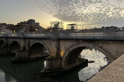 A bridge across the Tiber at sunset, scaffolding covering the statues on either side. 