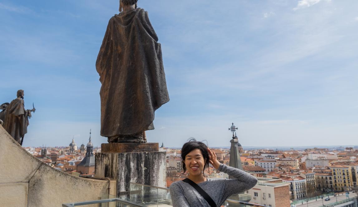 A student looks out over the Madrid, Spain cityscape. Next to her is a statue.