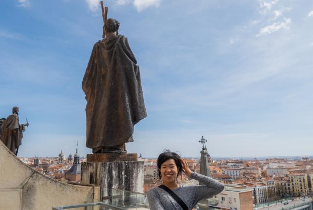A student looks out over the Madrid, Spain cityscape. Next to her is a statue.