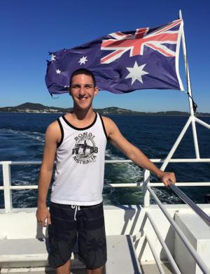 a student poses for a photo while on a boat with the Australian flag blowing behind them