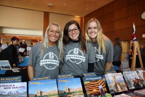 three students standing in front of fair table with IES Abroad catalogs